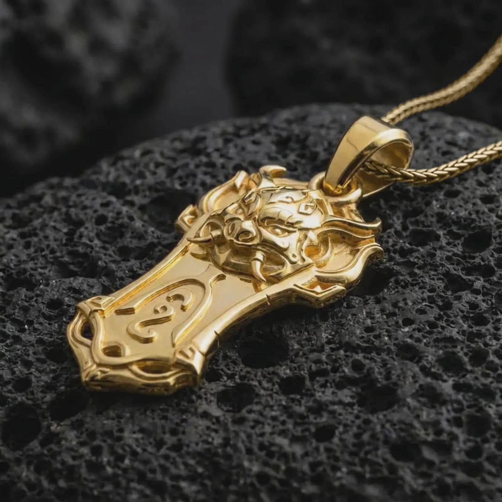 A gold plated Taurus bull pendant lies on textured volcanic rock in a dramatic studio macro shot, highlighting the bold strength symbol design.