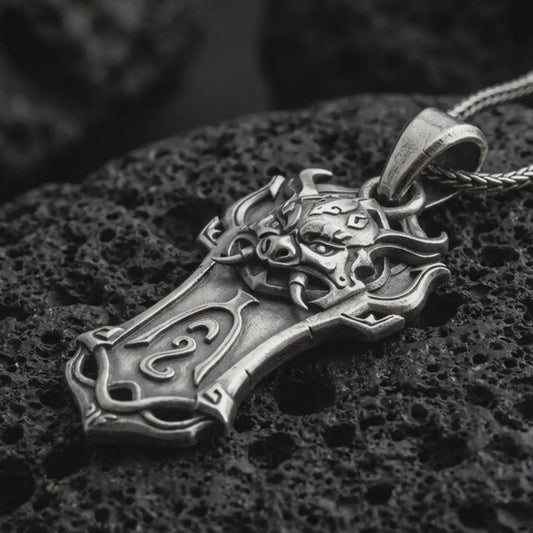 An oxidized Taurus bull pendant rests on dark volcanic rock in a macro studio close-up, showing a horned animal head over a shield-inspired frame.