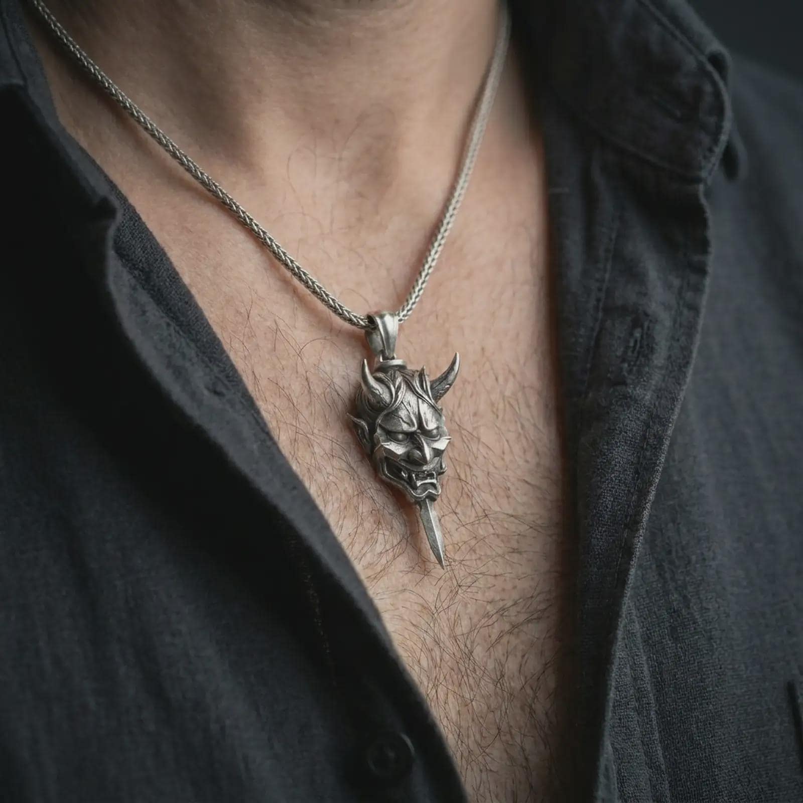 An oxidized oni mask pendant is worn on the neck in a close-up lifestyle shot, centered on the chest as a fierce Japanese warrior amulet.