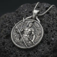 Load image into Gallery viewer, An oxidized Spartan warrior pendant rests on dark volcanic rock in a macro studio close-up, showing a detailed Greek soldier with spear and laurel frame.
