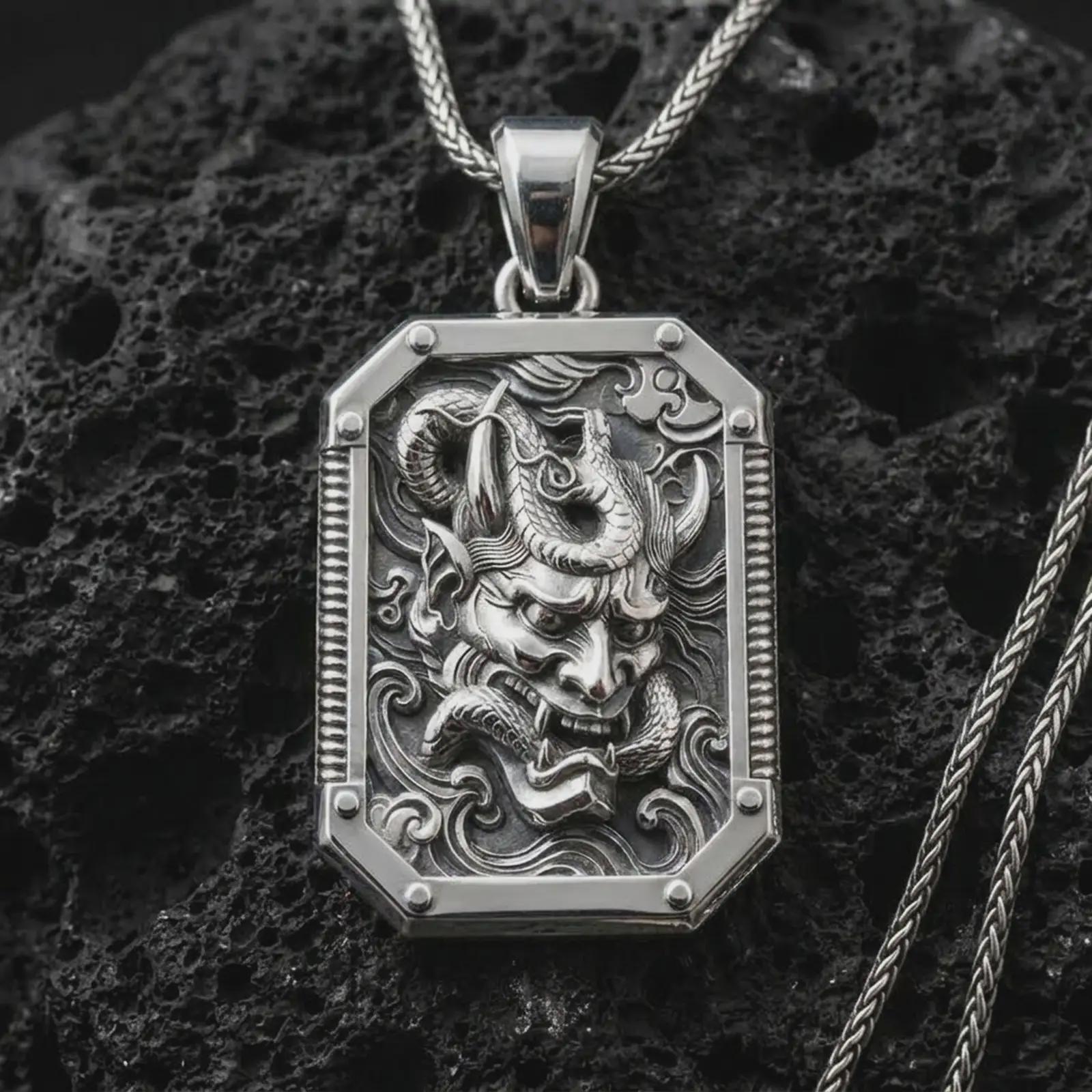 A polished silver Hannya mask pendant is displayed on black volcanic rock in a premium macro studio close-up with sharp horned mask details.
