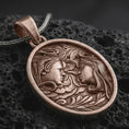 Load image into Gallery viewer, An Bronze Gemini pendant rests on dark volcanic rock in a macro studio close-up, showing two facing figures with floral details and a symbolic twin design.
