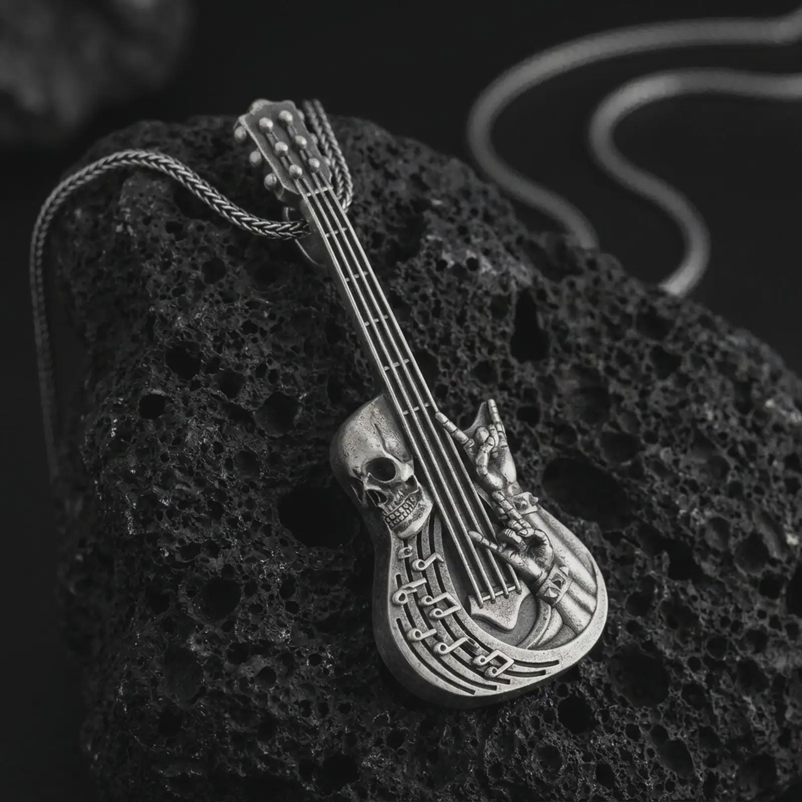 Oxidized skull guitar pendant necklace on textured volcanic rock, close-up studio shot highlighting the guitar body, skull detail, rock hand gesture, music notes, and antique silver contrast.