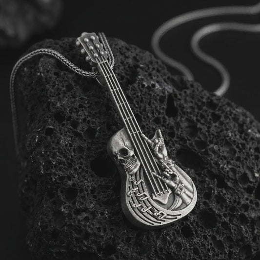 Oxidized skull guitar pendant necklace on textured volcanic rock, close-up studio shot highlighting the guitar body, skull detail, rock hand gesture, music notes, and antique silver contrast.