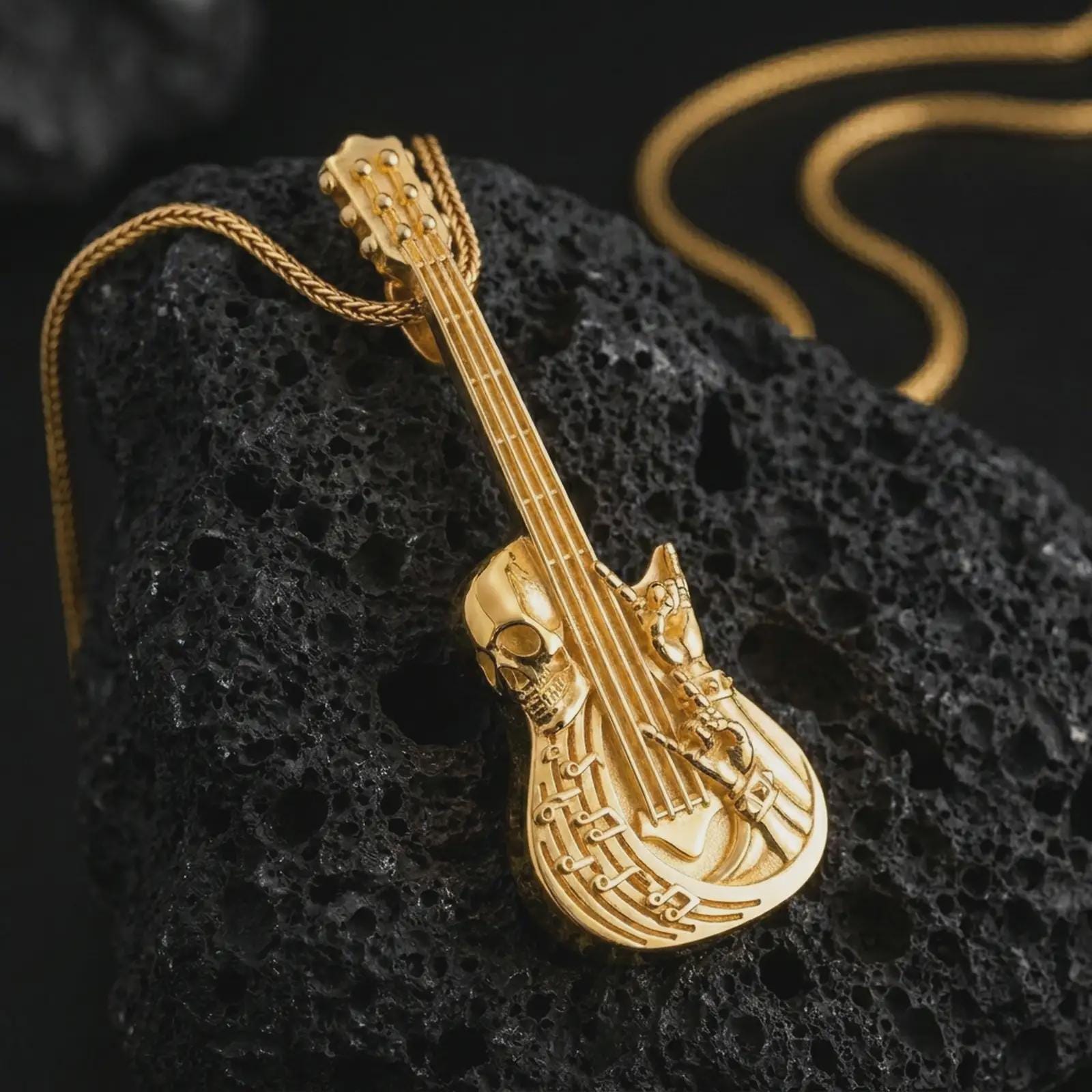 Gold plated skull guitar pendant necklace on textured volcanic rock, premium close-up studio composition emphasizing the electric guitar shape, skull motif, and rock and roll symbolism.