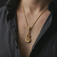 Load image into Gallery viewer, Gold plated skull guitar pendant necklace worn on the chest, premium lifestyle jewelry photo with the gothic guitar pendant centered on a spiga chain.
