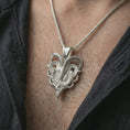 Load image into Gallery viewer, Polished silver biomechanical ram skull pendant necklace worn on the chest, masculine lifestyle shot highlighting the polished horn structure, skull relief, and bright silver finish.
