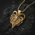 Load image into Gallery viewer, Gold plated biomechanical ram skull pendant necklace on textured volcanic rock, premium close-up studio composition emphasizing the mechanical ram skull, spiral horns, and gothic talisman design.
