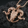 Load image into Gallery viewer, Rose gold plated ram skull pendant necklace on textured volcanic rock, detailed macro product shot with soft warm reflections and bold gothic ram skull design.
