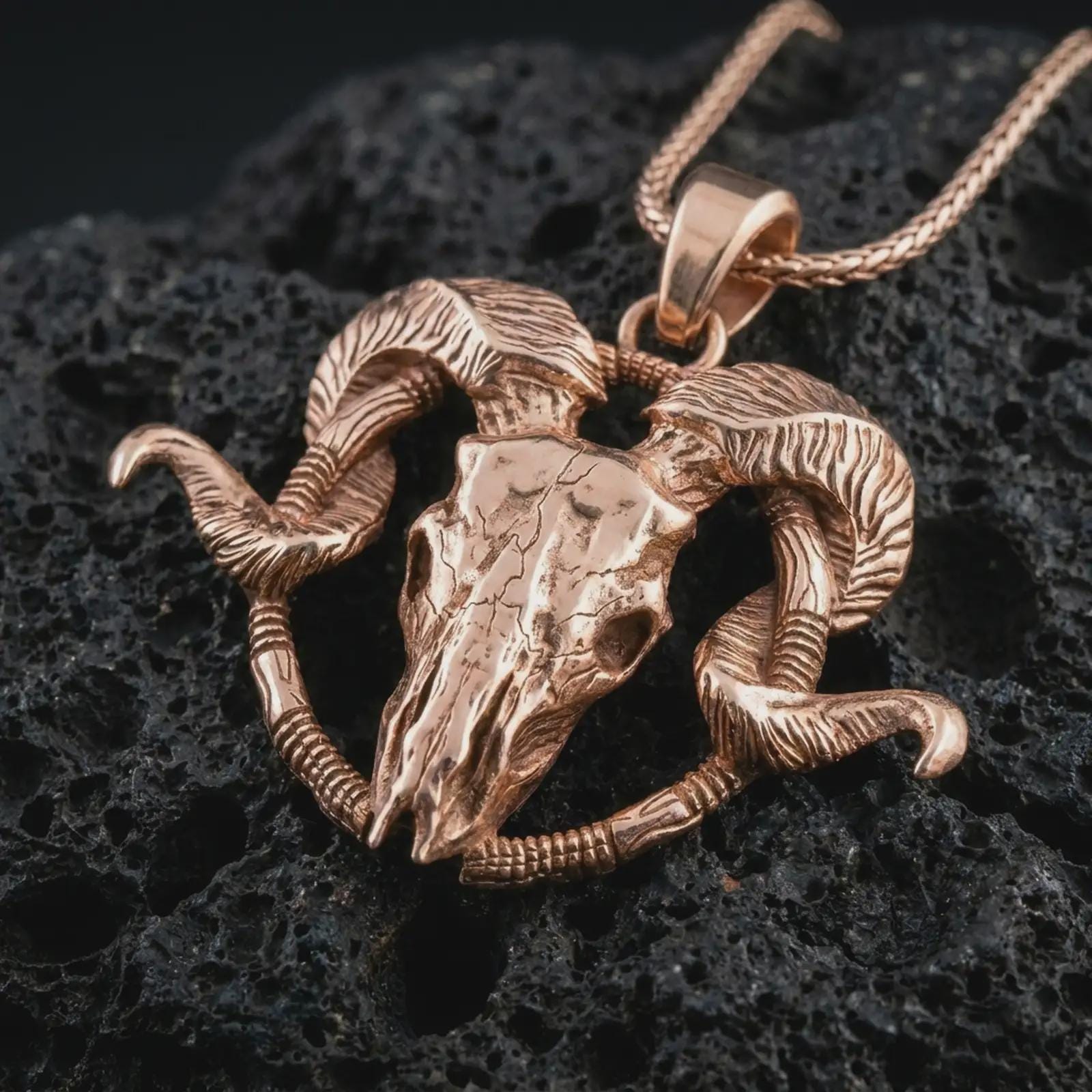 Rose gold plated ram skull pendant necklace on textured volcanic rock, detailed macro product shot with soft warm reflections and bold gothic ram skull design.