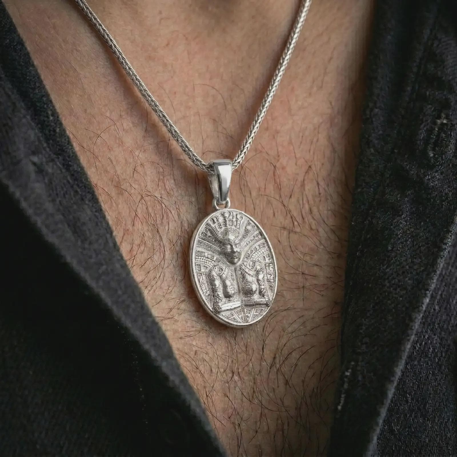 A polished silver Aztec mask pendant is worn on the neck in a premium close-up lifestyle image, showing the detailed tribal mask motif clearly.