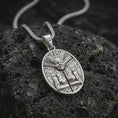 Load image into Gallery viewer, A polished silver Aztec mask pendant is displayed on black volcanic rock in a premium macro studio close-up with geometric Mayan-inspired engraving.
