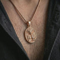 Load image into Gallery viewer, A rose gold plated Aztec mask pendant is worn on the neck in a close-up lifestyle composition, highlighting its geometric tribal pattern and bold oval shape.
