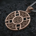 Load image into Gallery viewer, Bronze Celtic cross pendant necklace on textured volcanic rock, close-up studio shot highlighting the circular cross shape, Norse knotwork pattern, openwork details, and antique silver contrast.
