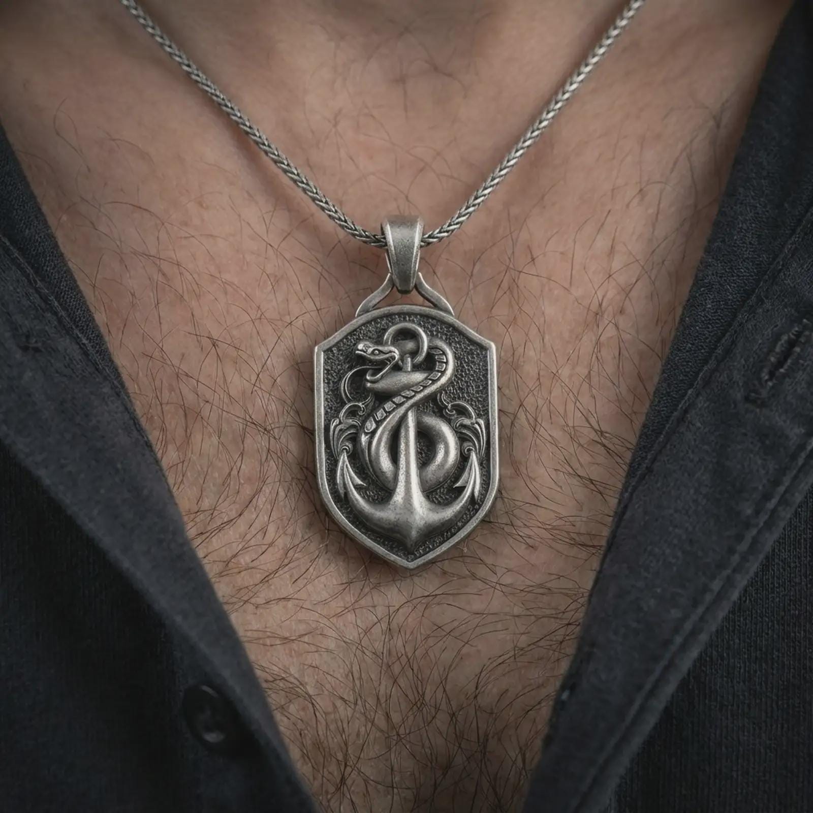 Oxidized serpent and anchor pendant necklace worn on the chest, close-up lifestyle jewelry photo showing the nautical amulet on a spiga chain with dark clothing.