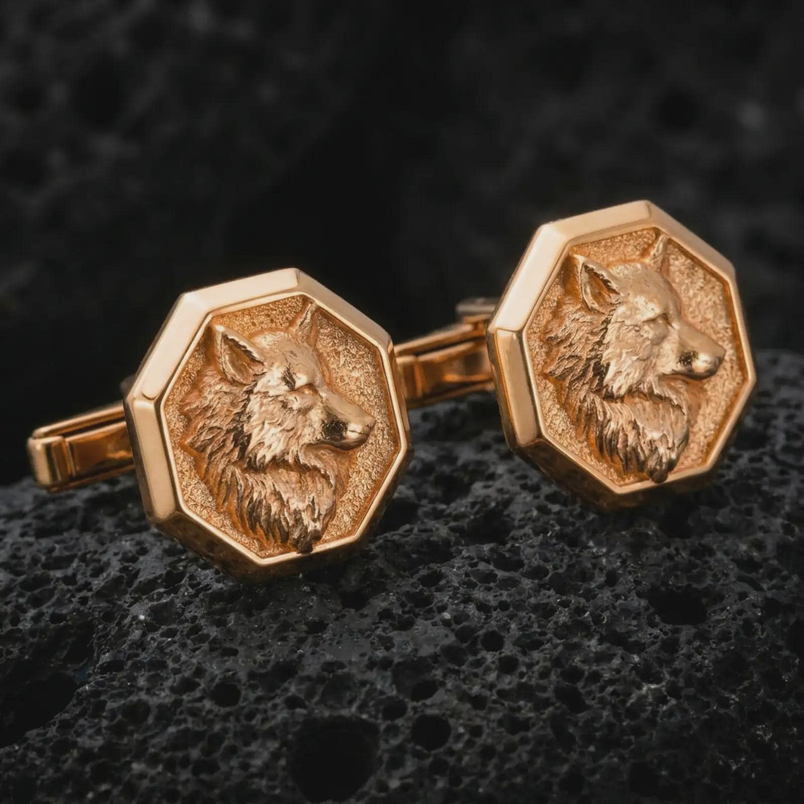 Rose gold plated wolf head cufflinks are photographed on porous volcanic rock in a close-up studio composition with refined luxury lighting.