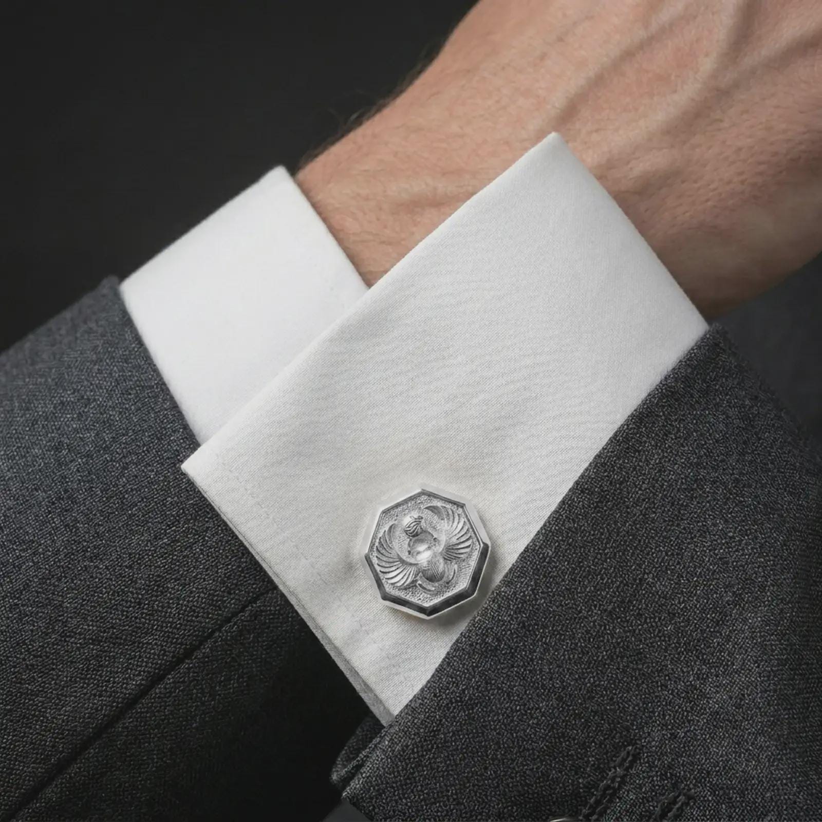 A polished silver scarab cufflink is worn on a shirt cuff in a premium close-up lifestyle image, showing the winged beetle design clearly.