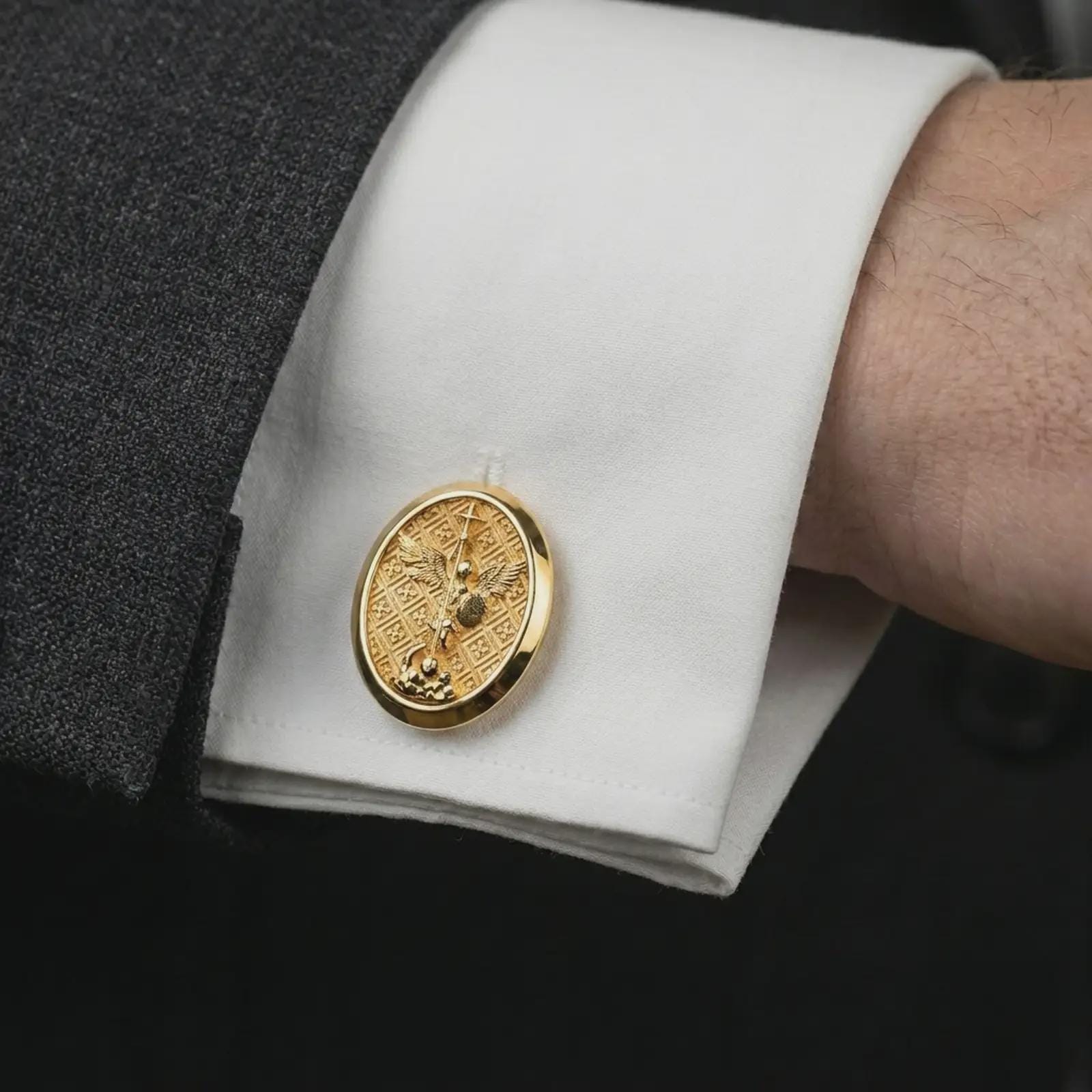 Gold plated Saint Michael cufflinks worn on a suit cuff, premium lifestyle photo with the protective Saint Michael design clearly visible on formal attire.