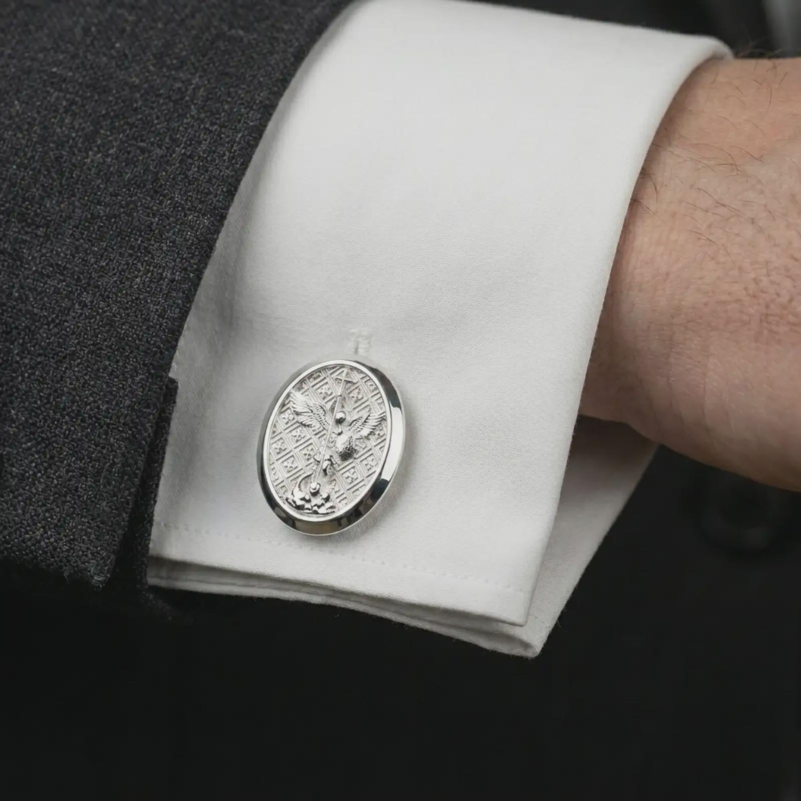 Polished silver Saint Michael cufflinks worn on a suit cuff, masculine formalwear shot highlighting the bright silver finish, oval frame, and archangel relief.