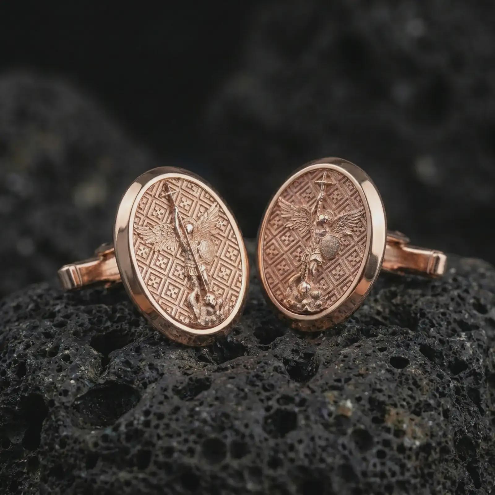 Rose gold plated Saint Michael cufflinks on textured volcanic rock, detailed macro product shot with soft warm reflections and protective Christian symbolism.