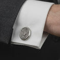 Load image into Gallery viewer, Oxidized Saint Michael cufflinks worn on a suit cuff, close-up lifestyle jewelry photo showing the guardian angel medal design with crisp white shirt fabric.
