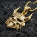 Load image into Gallery viewer, A gold plated Surtur pendant lies on textured volcanic rock in a dramatic studio macro shot, highlighting the horned mask motif and Ragnarok-inspired style.
