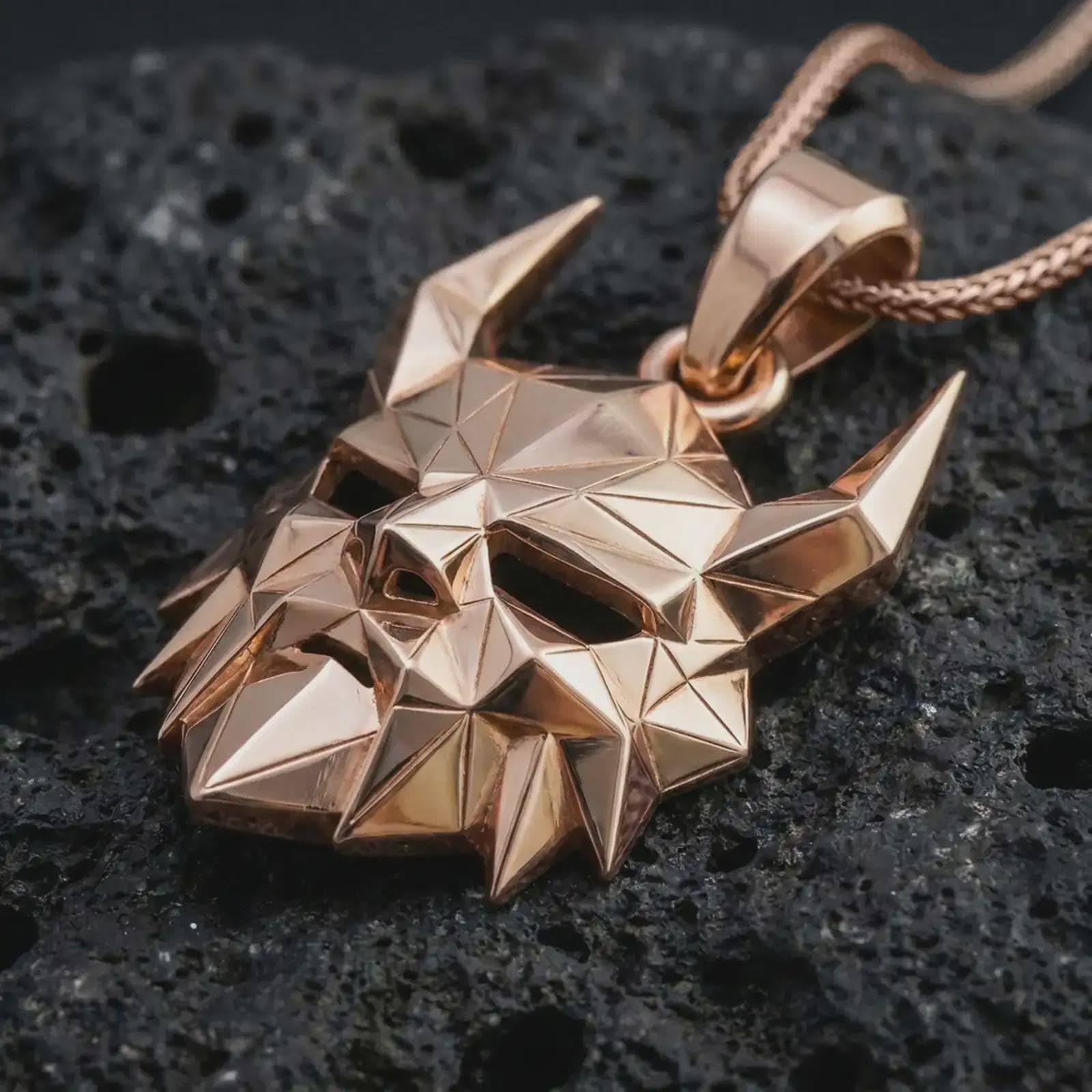 A rose gold plated Surtur pendant is photographed on porous volcanic rock in a close-up studio composition with refined luxury lighting and faceted sculptural detail.