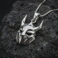 Load image into Gallery viewer, A polished silver Loki pendant is displayed on black volcanic rock in a premium macro studio close-up with sharp geometric planes and bold mask detail.
