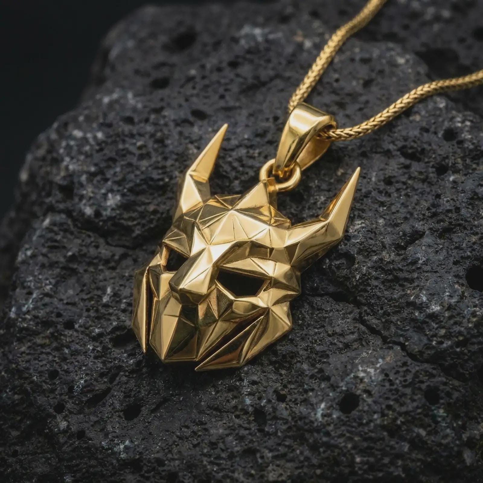 A gold plated Loki pendant lies on textured volcanic rock in a dramatic studio macro shot, highlighting the horned trickster mask design.