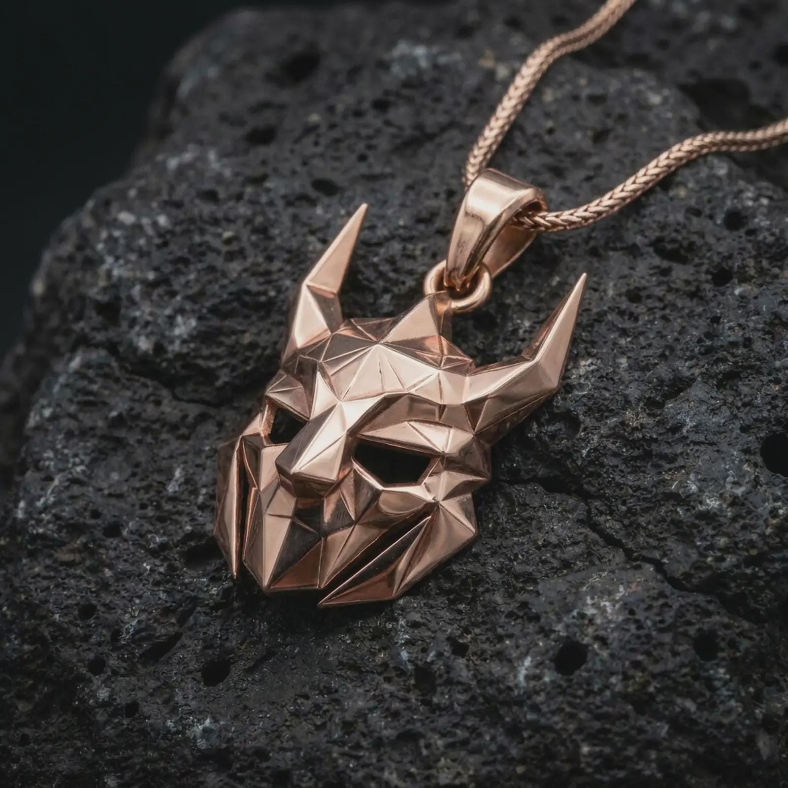 A rose gold plated Loki pendant is photographed on porous volcanic rock in a close-up studio composition with refined luxury lighting and angular sculptural detail.