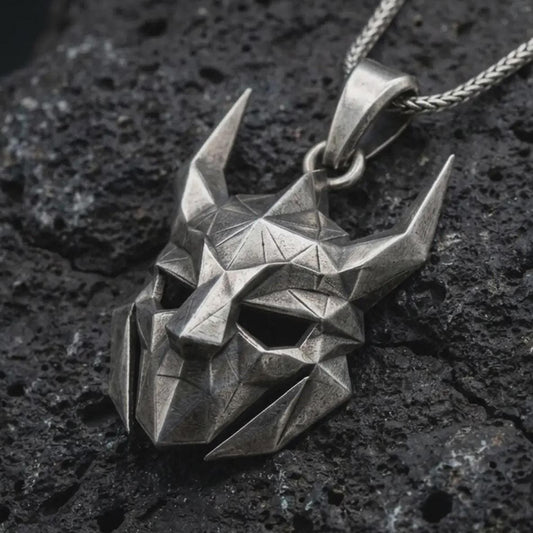 An oxidized Loki pendant rests on dark volcanic rock in a macro studio close-up, showing a faceted horned mask inspired by Norse mythology.