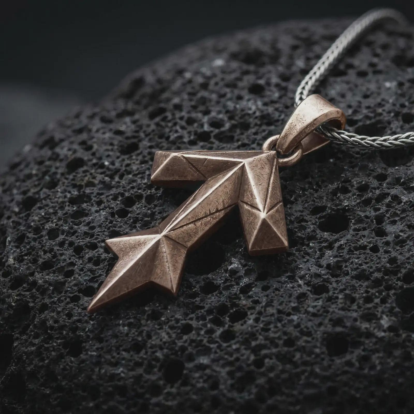 A Bronze Tyr rune pendant rests on dark volcanic rock in a macro studio close-up, showing the Teiwaz symbol in a bold geometric Norse design.