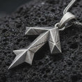 Load image into Gallery viewer, An oxidized Tyr rune pendant rests on dark volcanic rock in a macro studio close-up, showing the Teiwaz symbol in a bold geometric Norse design.
