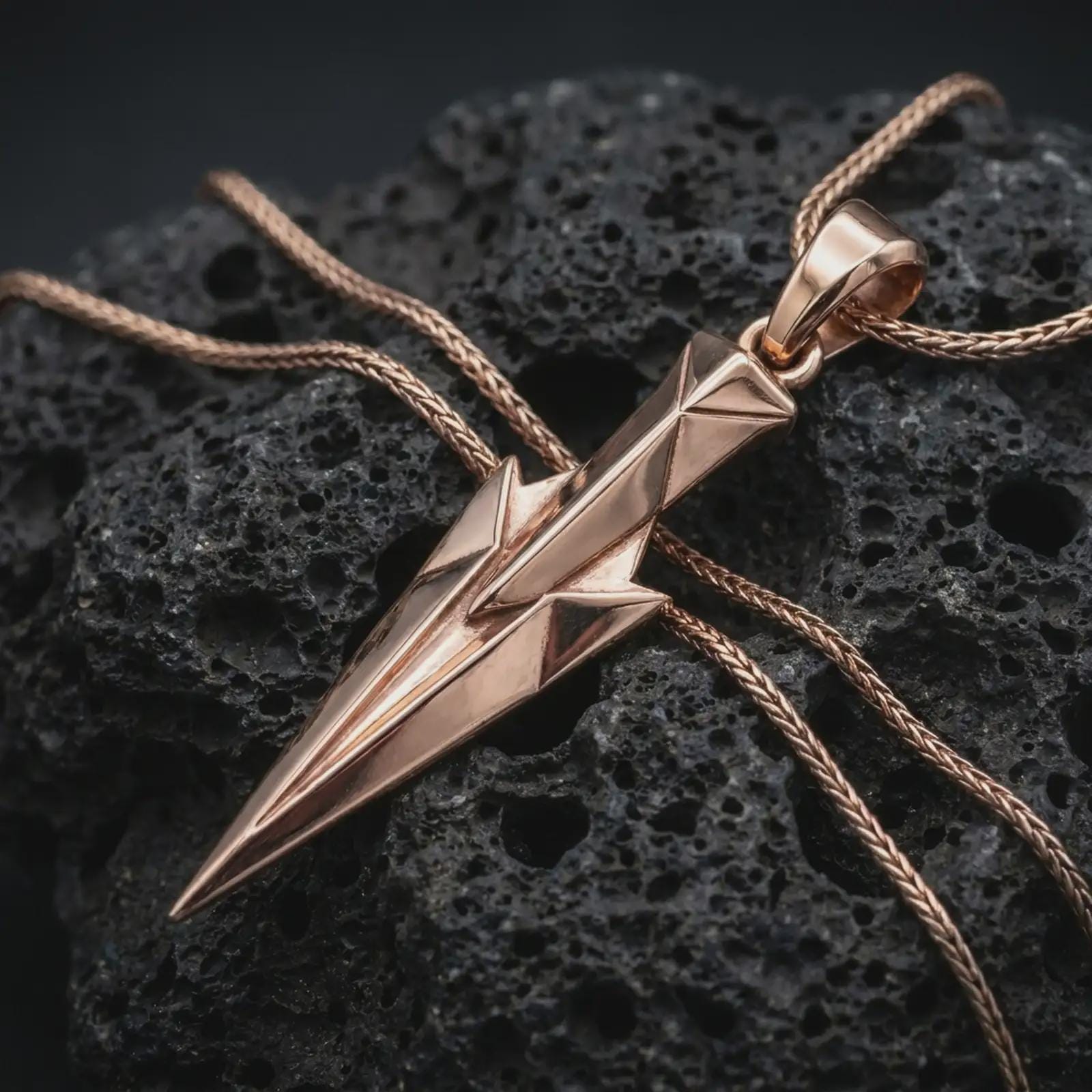 A rose gold plated Gungnir pendant is photographed on porous volcanic rock in a close-up studio composition with refined luxury lighting and faceted sculptural detail.