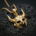 Load image into Gallery viewer, A gold plated Helm of Awe inspired mask pendant lies on textured volcanic rock in a dramatic studio macro shot, highlighting the Viking protection amulet design.

