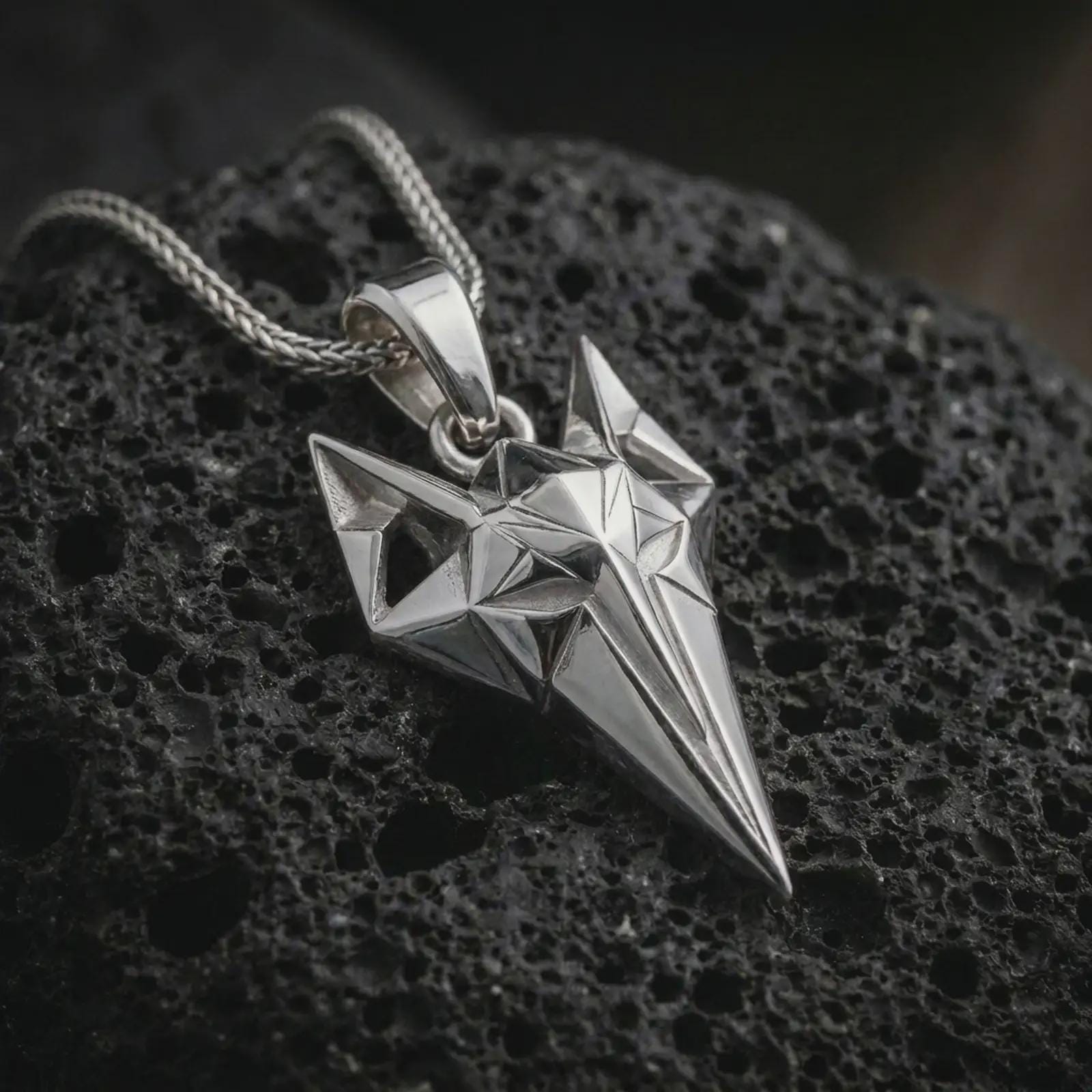 A polished silver Freyja cat pendant is displayed on black volcanic rock in a premium macro studio close-up with sharp geometric lines and bold feline detail.