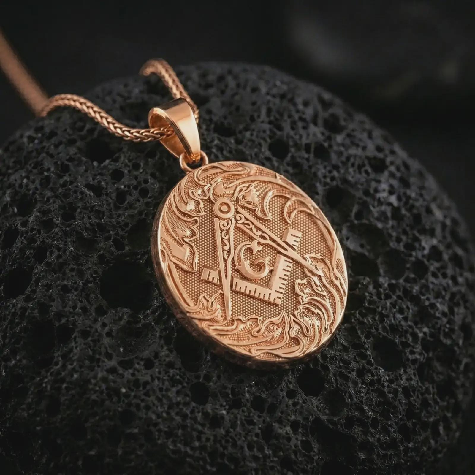 Gold plated Masonic square and compass pendant necklace on textured volcanic rock, premium close-up studio composition emphasizing the compass, square, circular medallion, and symbolic fraternal design.