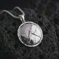 Load image into Gallery viewer, Polished silver Spartan shield pendant necklace on textured volcanic rock, centered macro jewelry photo with detailed warrior shield relief and bright silver highlights.
