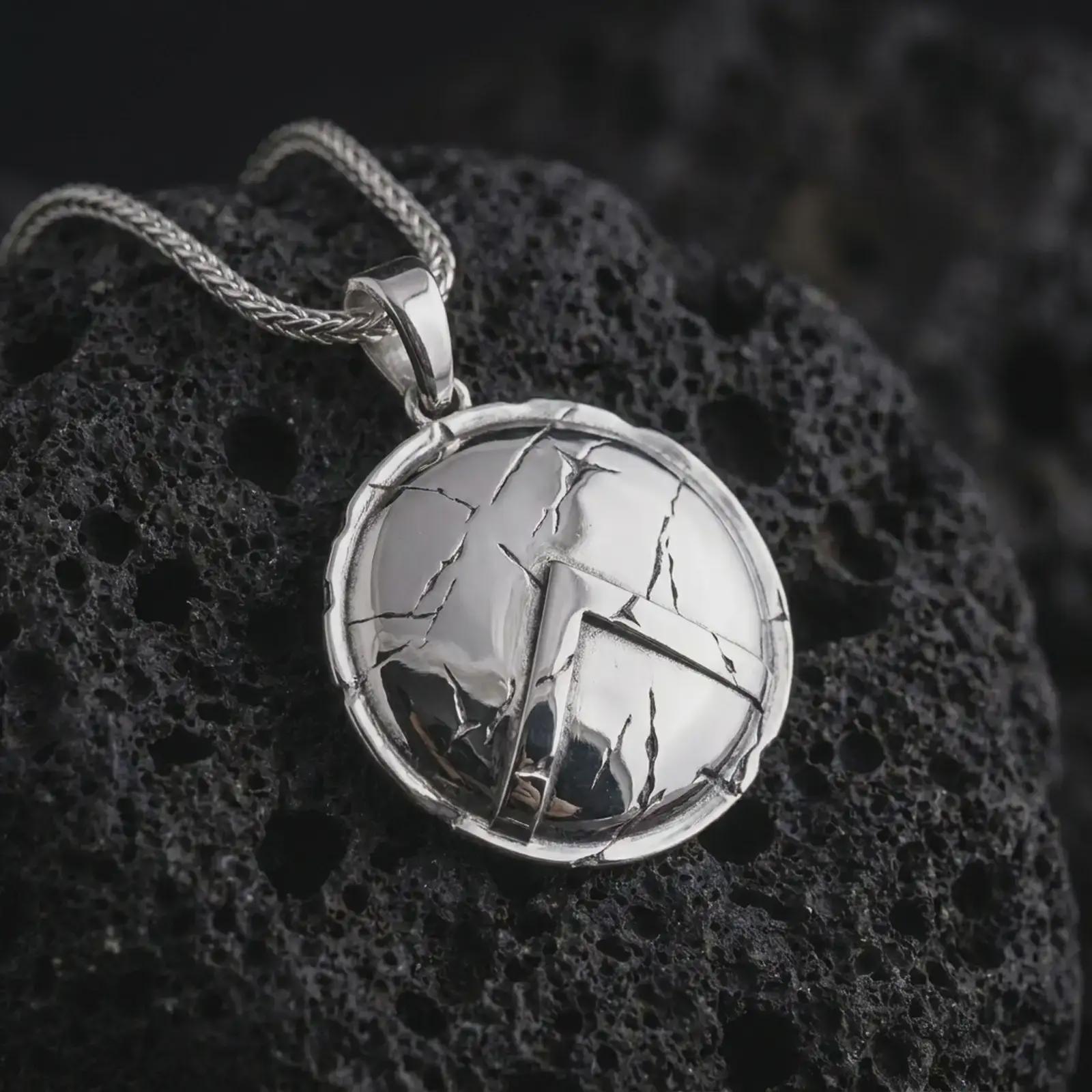 Polished silver Spartan shield pendant necklace on textured volcanic rock, centered macro jewelry photo with detailed warrior shield relief and bright silver highlights.