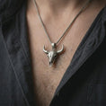 Load image into Gallery viewer, Oxidized bull skull pendant necklace worn on the chest, close-up lifestyle jewelry photo showing the western skull charm on a spiga chain with dark clothing.
