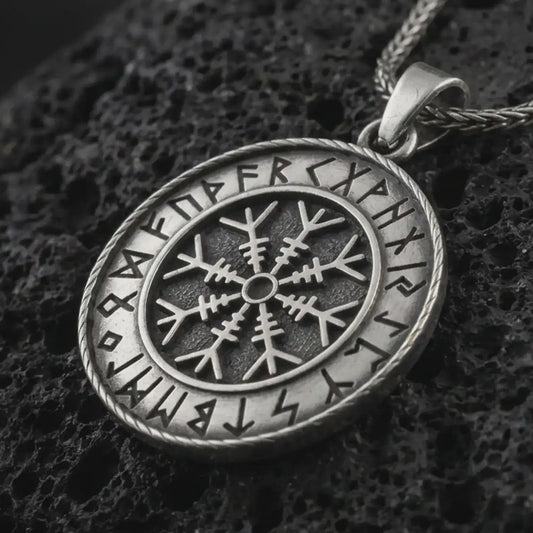Oxidized Vegvisir Viking rune pendant necklace on textured volcanic rock, close-up studio shot highlighting the Norse compass symbol, rune border, rope frame, and antique silver contrast.