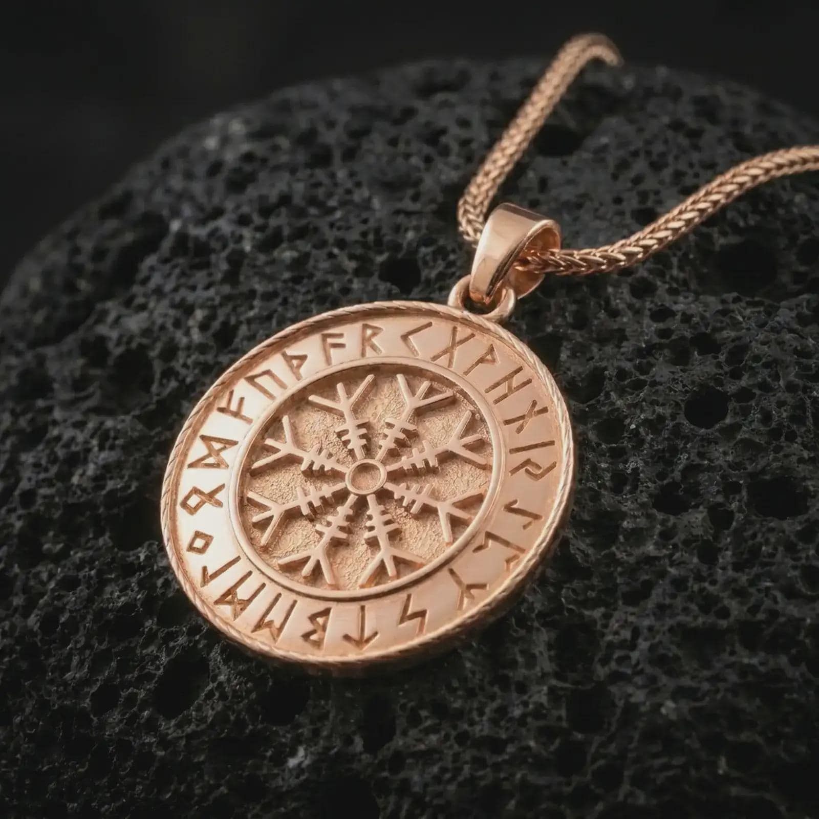 Rose gold plated Vegvisir Viking rune pendant necklace on textured volcanic rock, detailed macro product shot with soft warm reflections and symbolic Norse talisman styling.