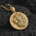 Load image into Gallery viewer, Gold plated Lion of Judah pendant necklace on textured volcanic rock, premium close-up studio composition emphasizing the regal lion head, radiant sunburst, and symbolic medallion design.

