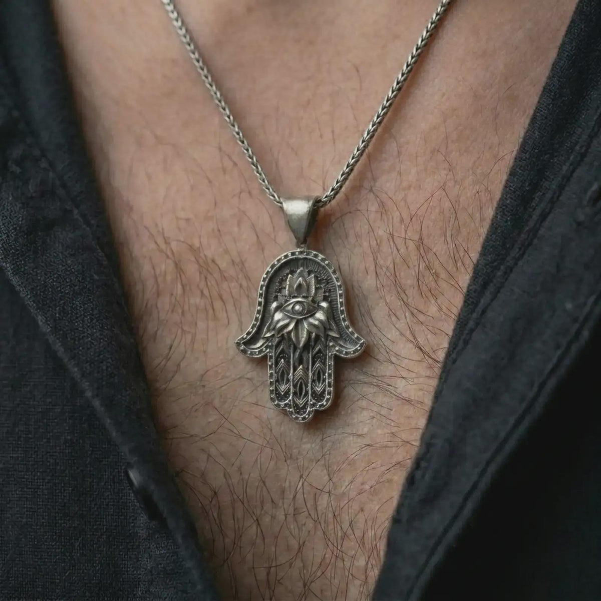 Oxidized hamsa hand pendant necklace worn on the chest, close-up lifestyle jewelry photo showing the protective evil eye amulet on a spiga chain with dark clothing.