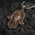 Load image into Gallery viewer, Bronze hamsa elephant pendant necklace on textured volcanic rock, close-up studio shot highlighting the elephant head relief, third eye symbol, beaded hand frame, and antique silver contrast.
