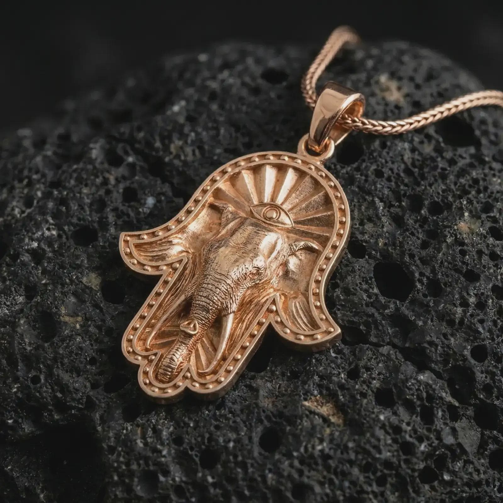Rose gold plated hamsa elephant pendant necklace on textured volcanic rock, detailed macro product shot with soft warm reflections and spiritual hamsa elephant styling.
