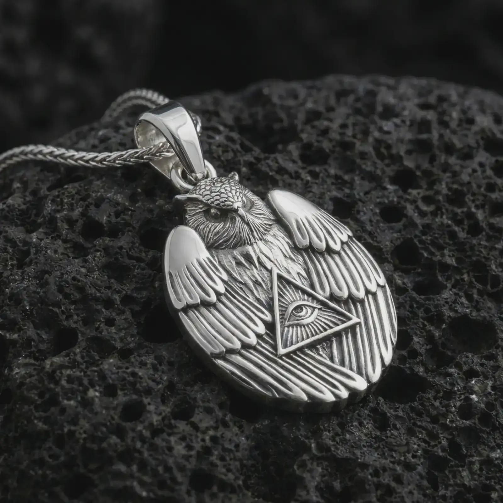 Polished silver owl all-seeing eye pendant necklace on textured volcanic rock, centered macro jewelry photo with detailed owl wings, sacred eye motif, and bright silver highlights.