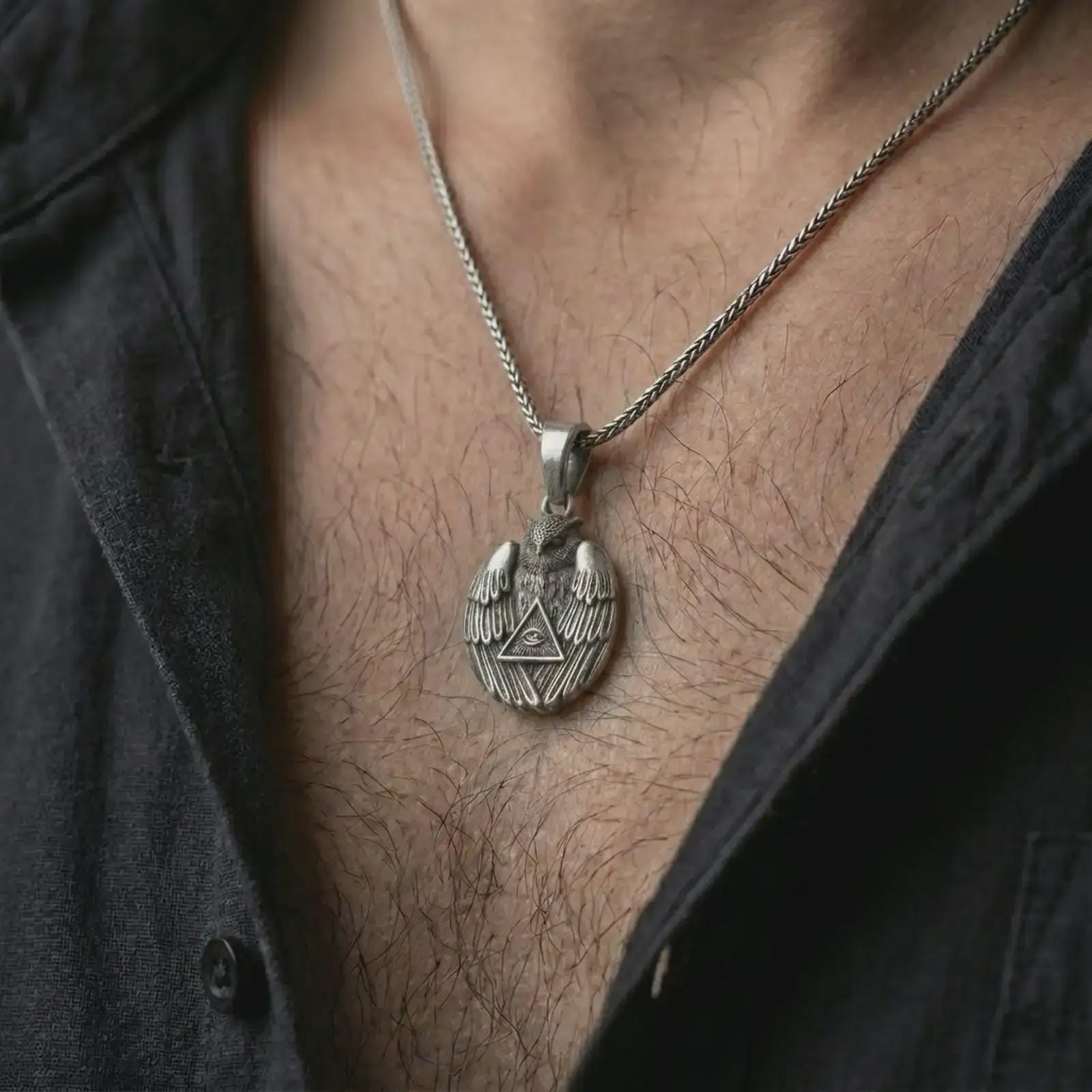Oxidized owl all-seeing eye pendant necklace worn on the chest, close-up lifestyle jewelry photo showing the mystical bird amulet on a spiga chain with dark clothing.