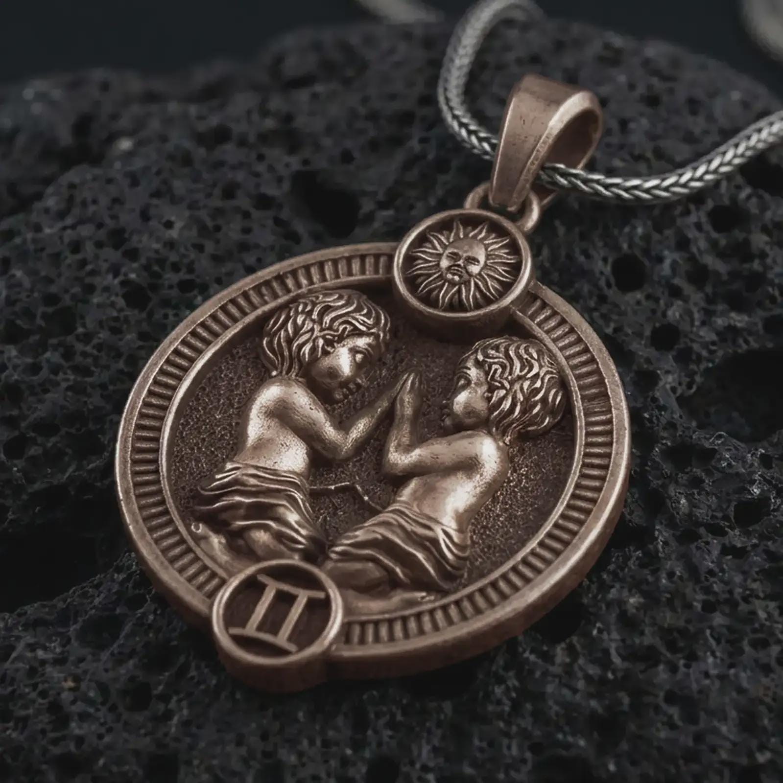 Bronze Gemini zodiac pendant necklace on textured volcanic rock, close-up studio shot highlighting the twin figures, sun detail, Gemini symbol, and antique silver contrast.