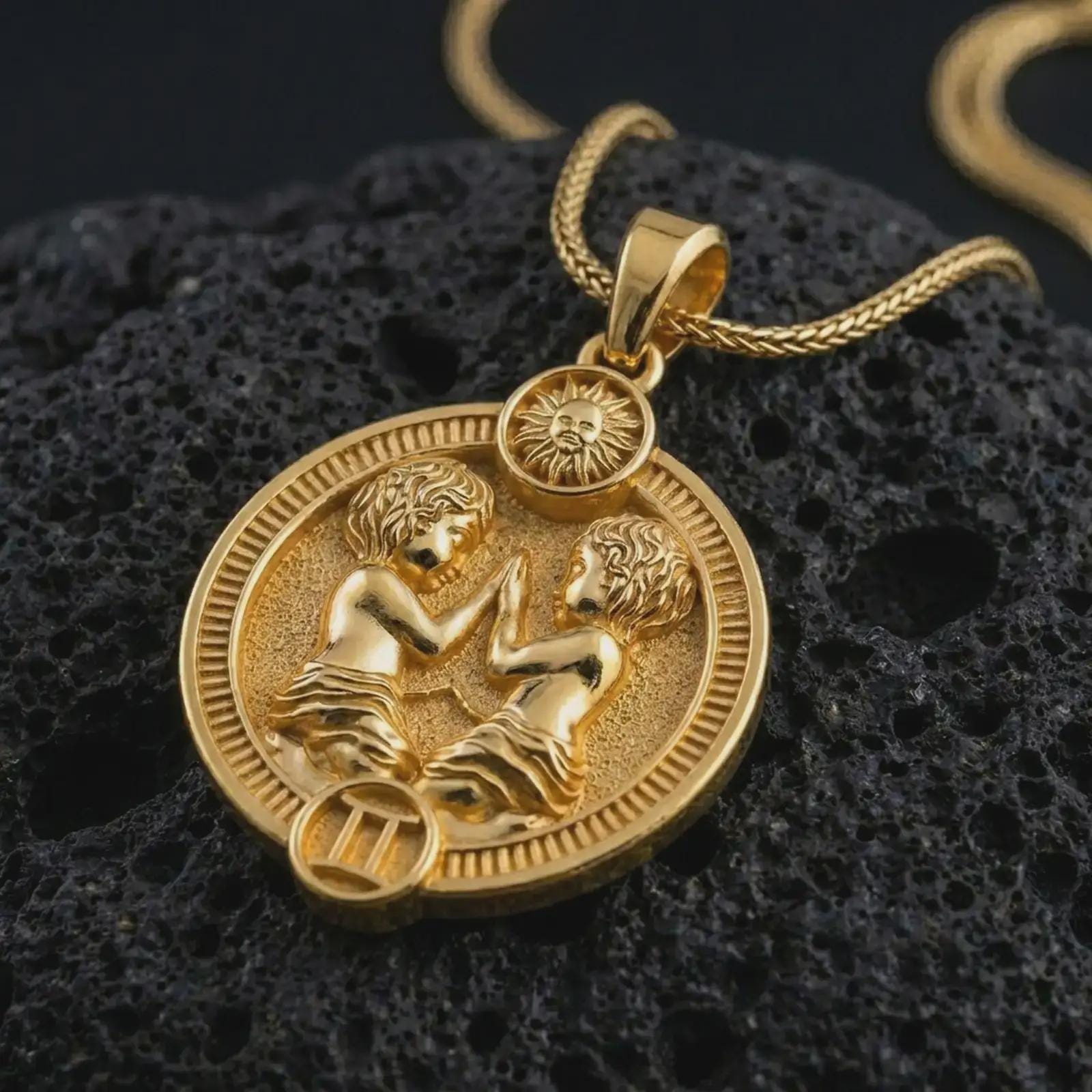 Gold plated Gemini zodiac pendant necklace on textured volcanic rock, premium close-up studio composition emphasizing the twin figures, sun motif, and astrology medallion design.